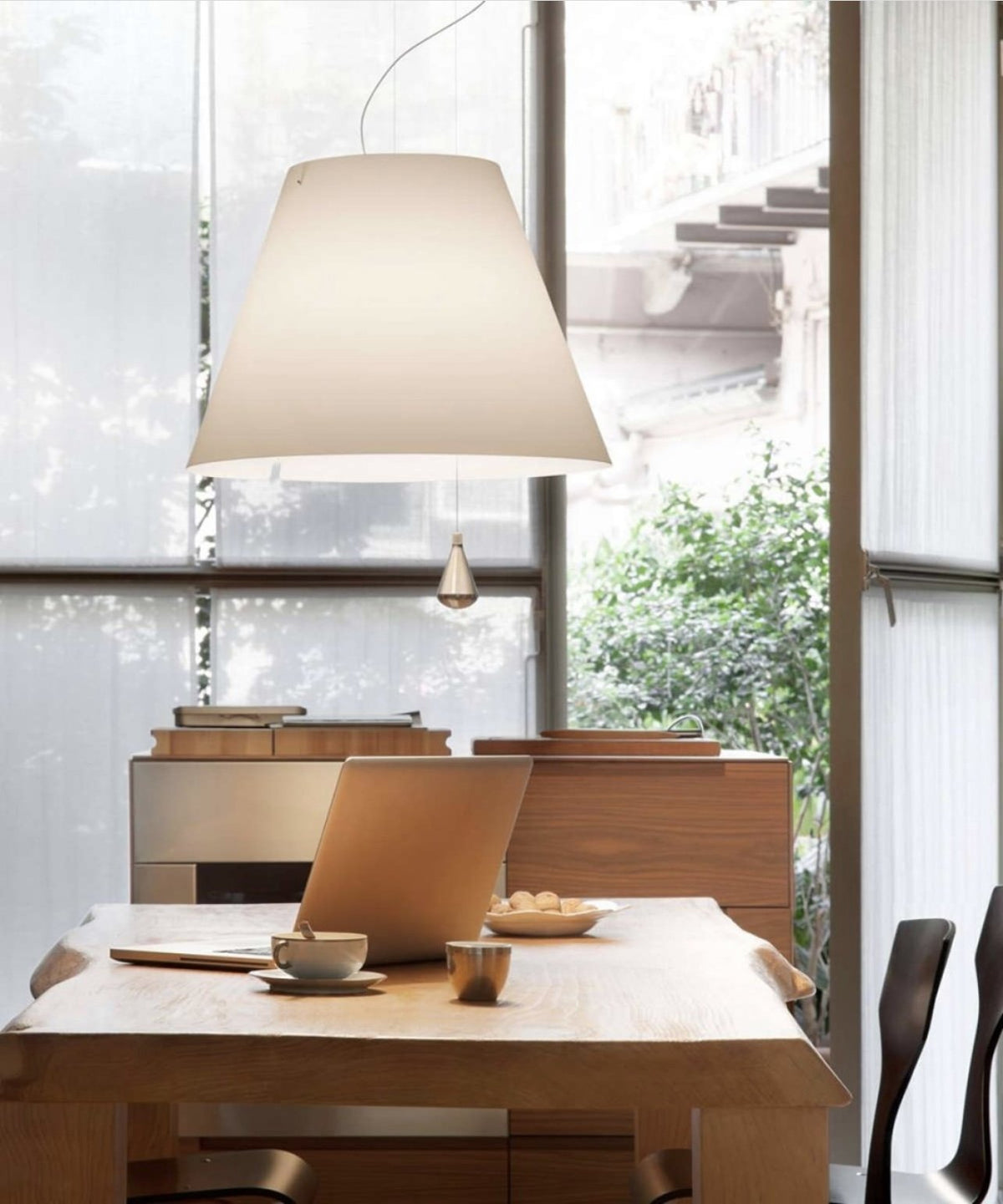 Luceplan Costanza Pendant with a white shade over a wooden work table