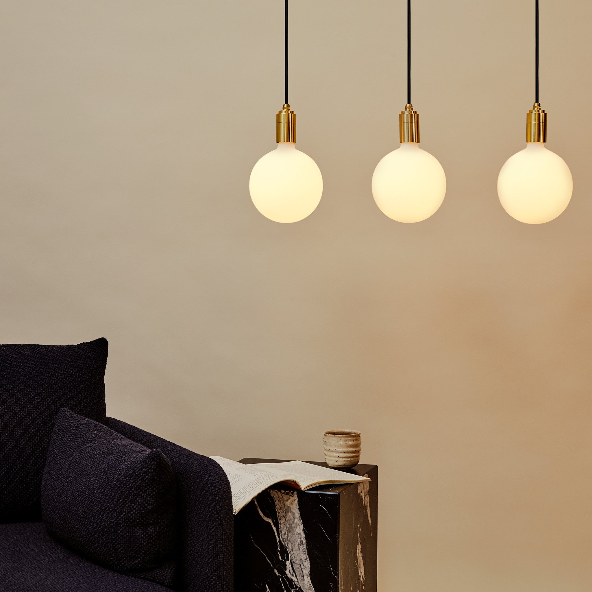 Tala Linear Triple Pendant in Brass with Sphere IV bulbs, styled above a sofa