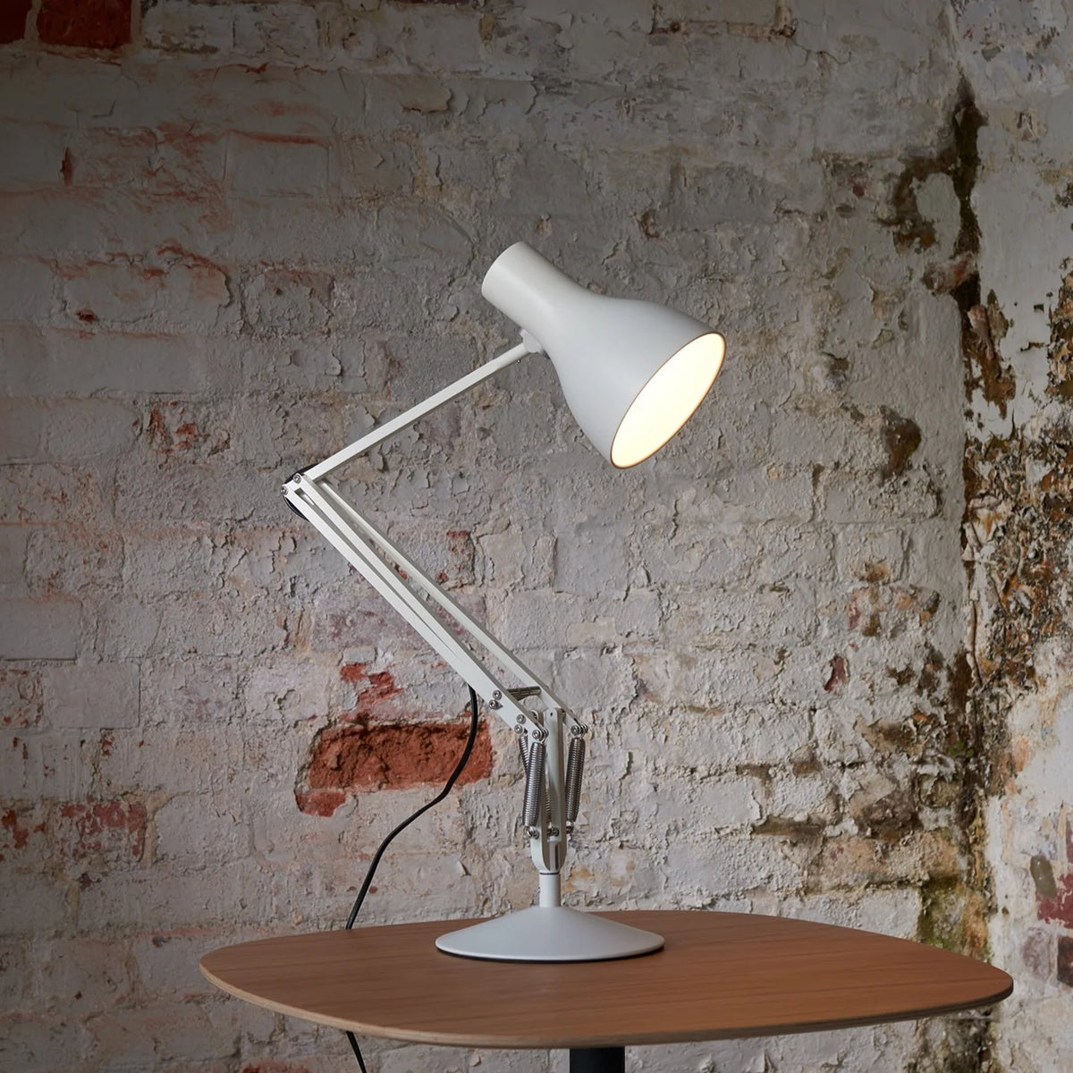 Anglepoise Type 75 desk lamp in Alpine White on a round wooden table against a weathered wall