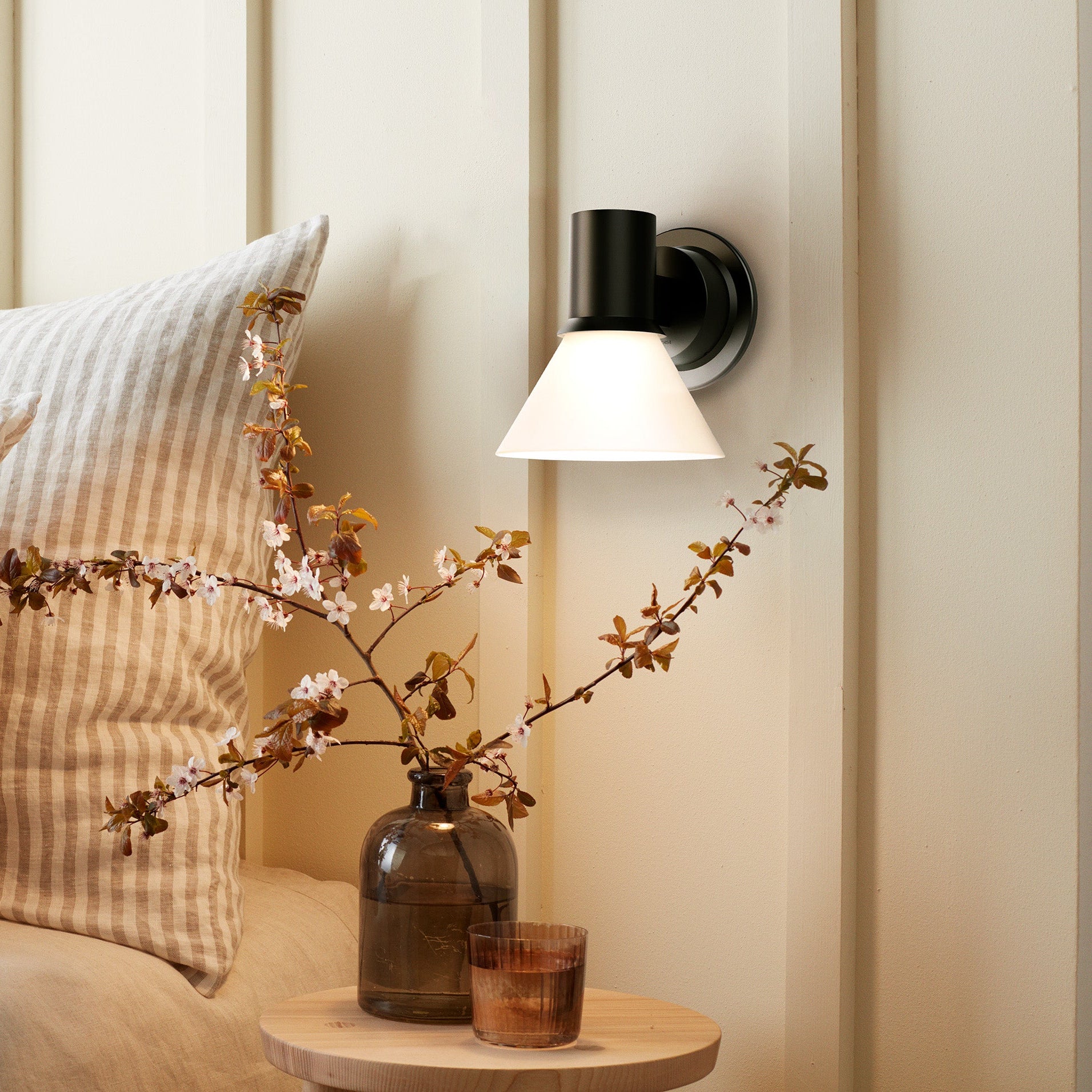 Bedroom scene with pillows, a lamp, and decorative branches on a nightstand.