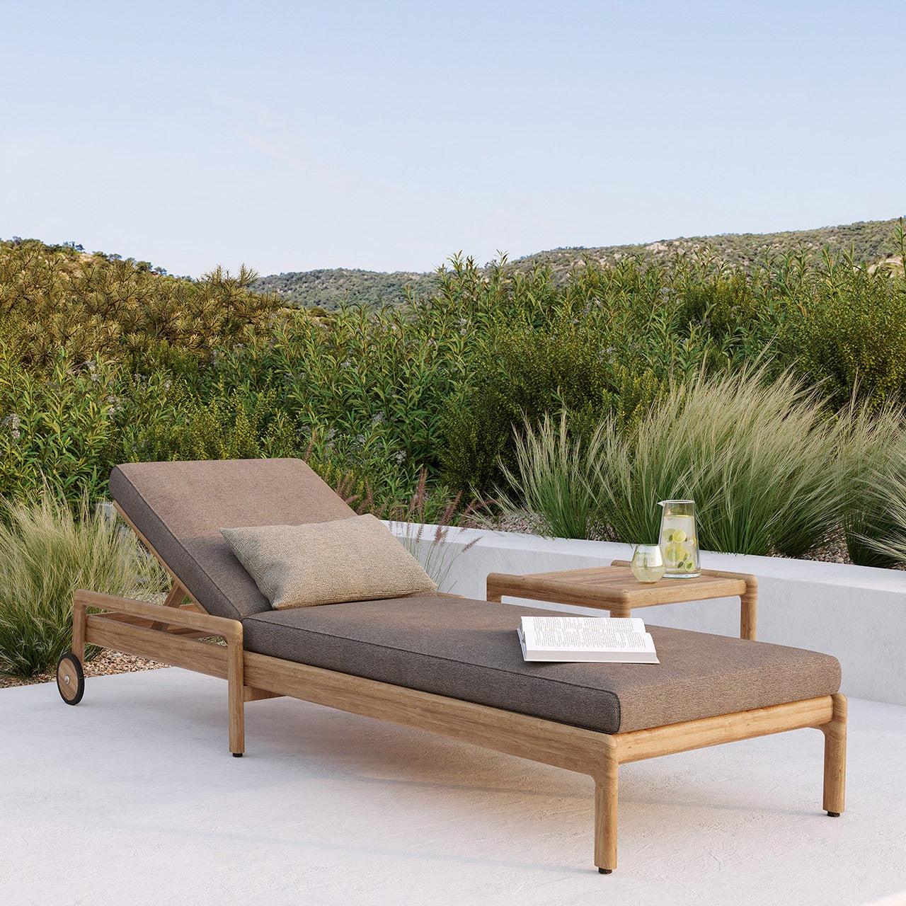 Ethnicraft Jack outdoor adjustable lounger in solid teak with a mocha quick-dry cushion, positioned on a sunlit terrace.