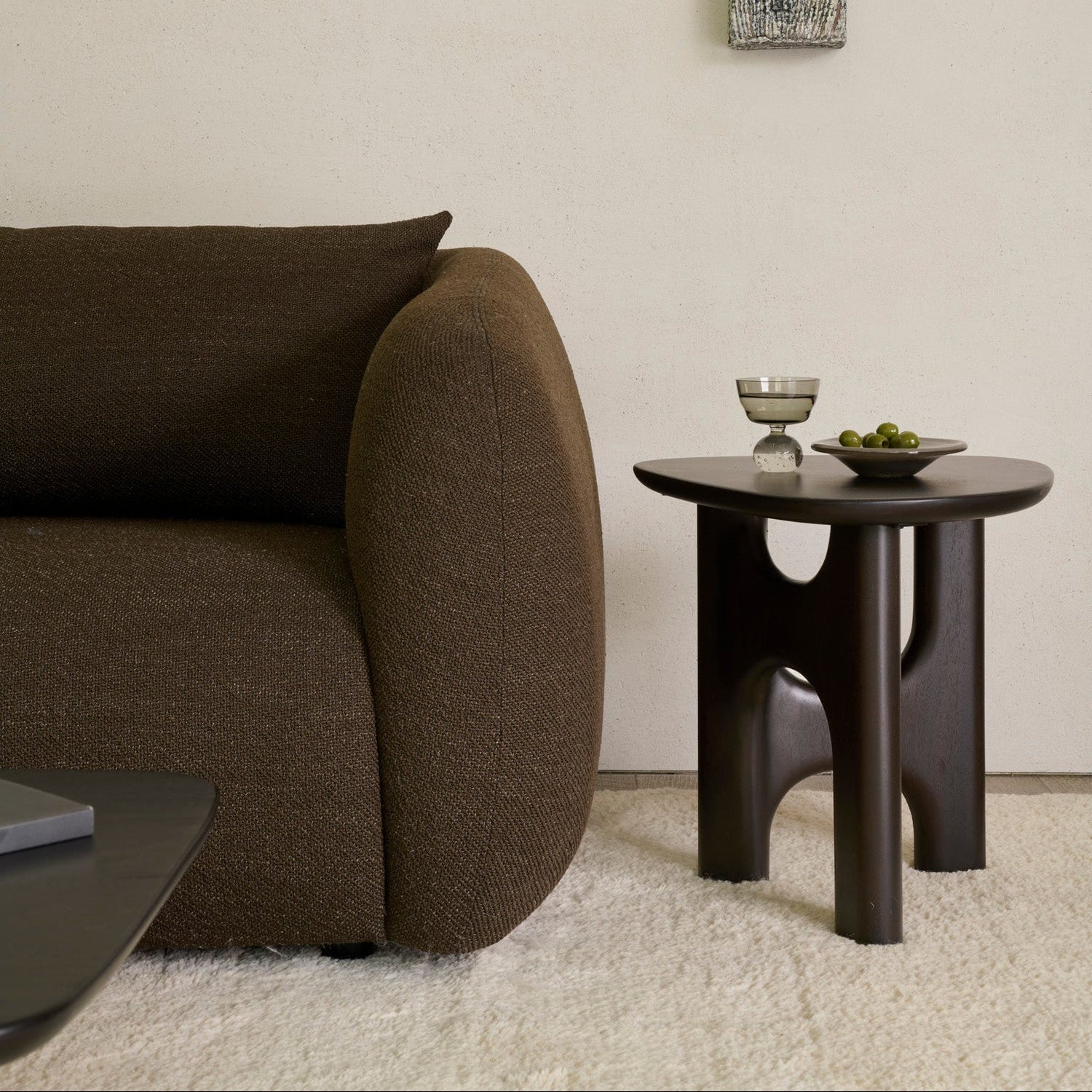 An Ethnicraft Flow side table in solid oak, styled beside a sofa and a wool rug in a living room.