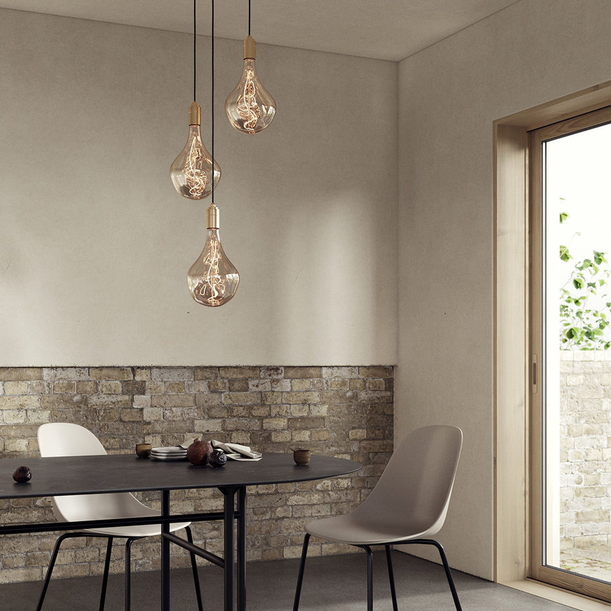 Tala Triple Pendant in brass with Voronoi II bulbs hanging above a wooden dining table in a dining room