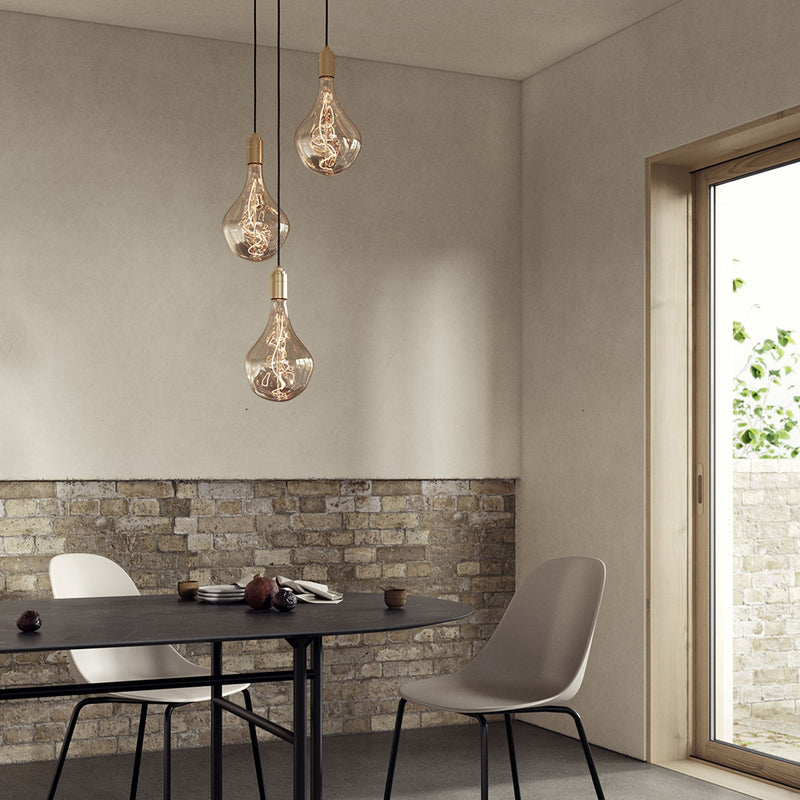 Tala Triple Pendant in brass with Voronoi II bulbs hanging above a wooden dining table in a dining room