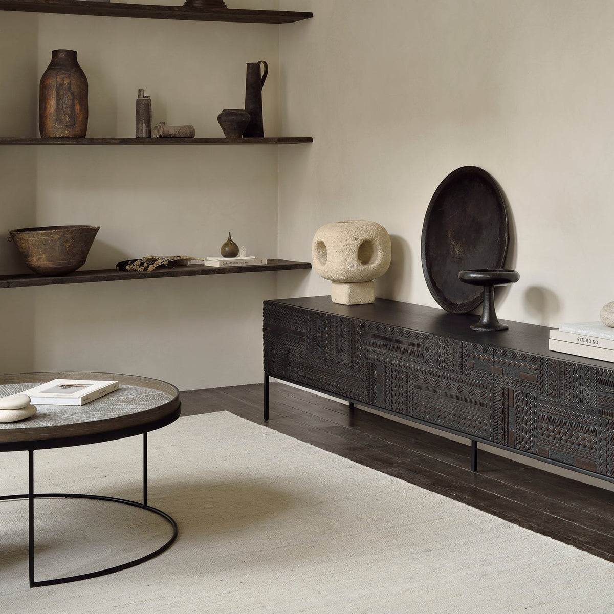A dark wood sideboard and wall shelves styled with ceramics in a warm neutral room