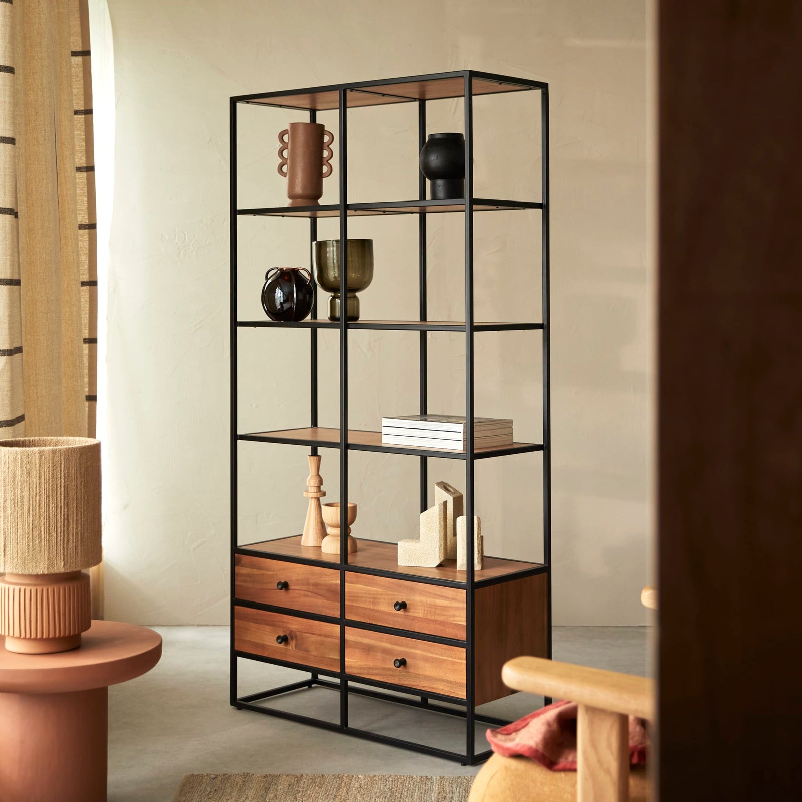 A black metal and wood shelving unit styled with ceramics and books in a warm interior