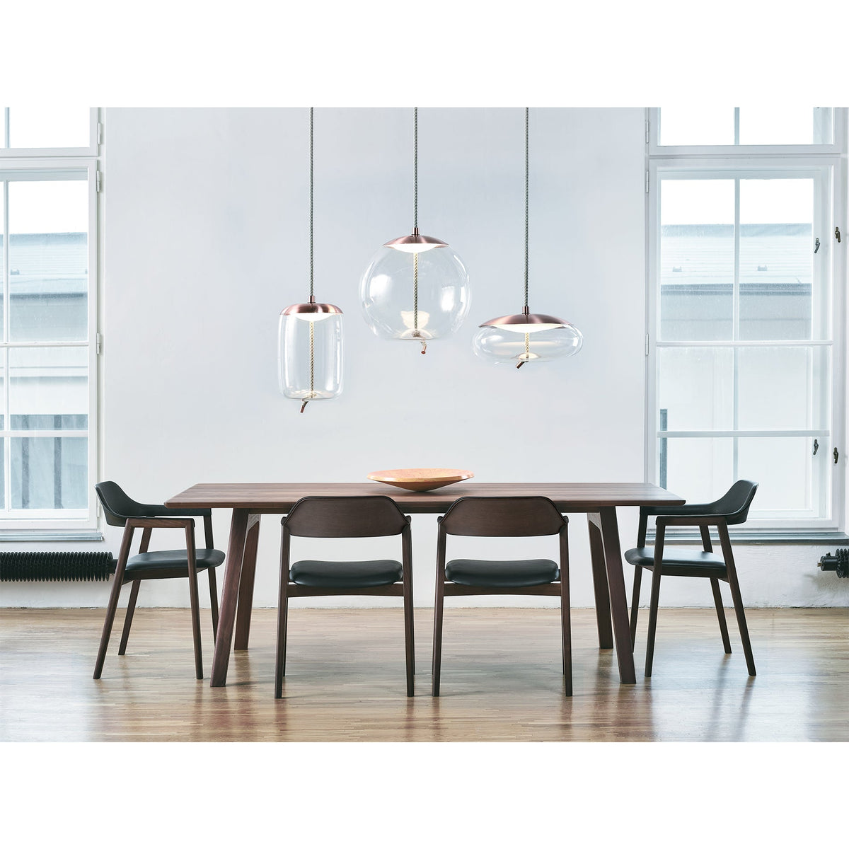 A dark wood dining table and chairs with clear glass pendants beside a window
