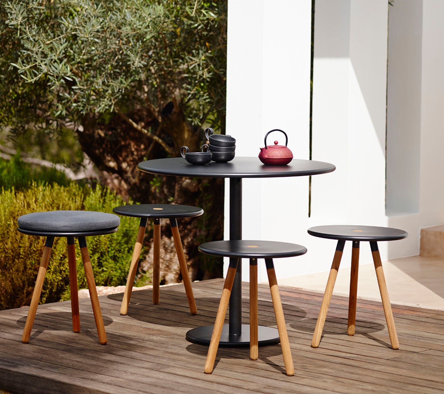 Outdoor setting with a round black table and four stools on a wooden deck.