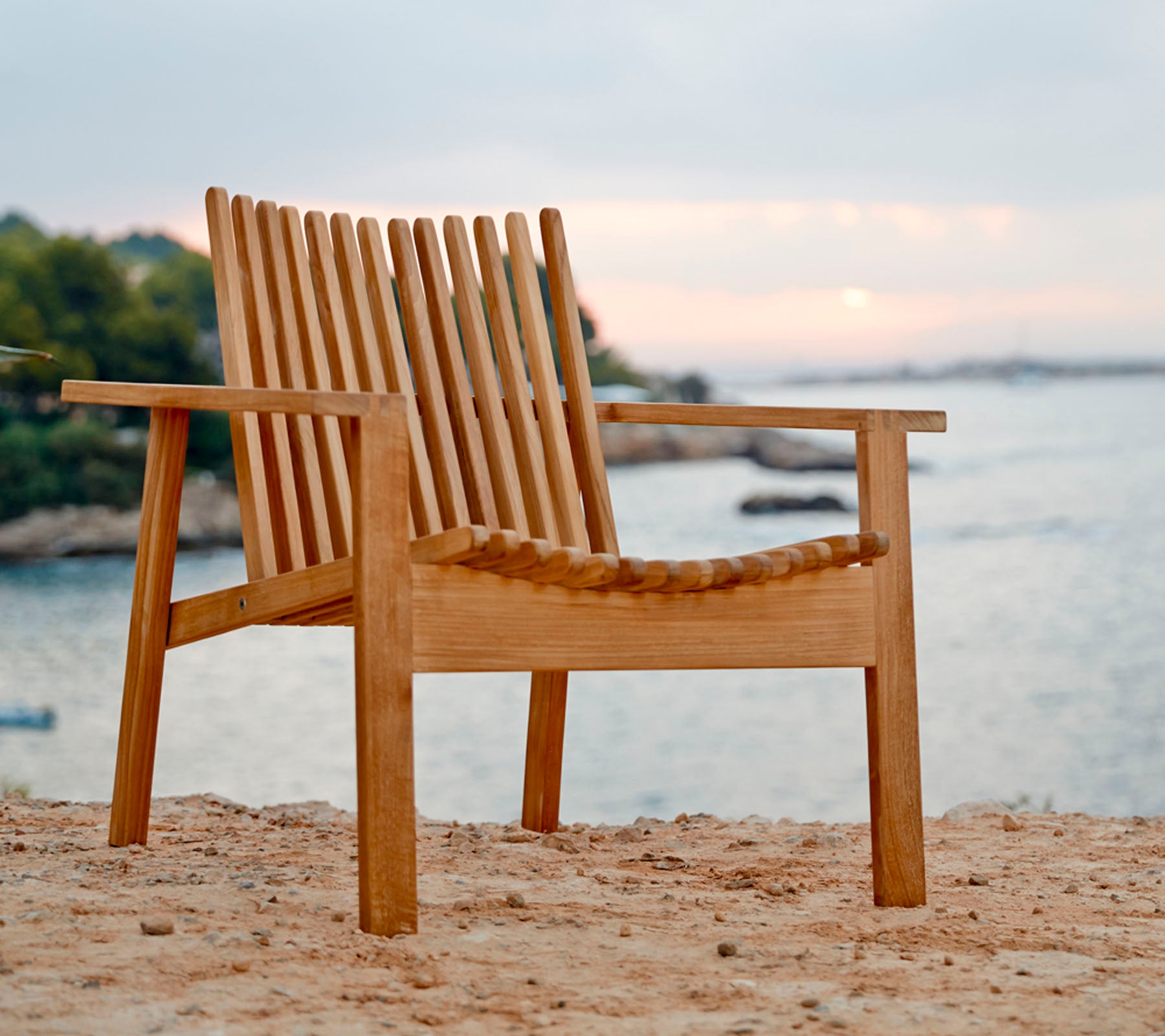 Wooden chair on a sandy beach with a blurred background of water and sky.
