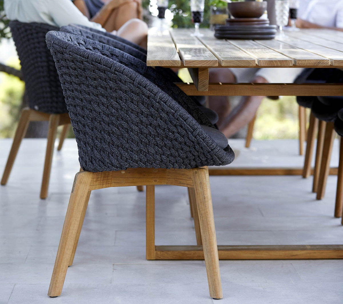 Detail of Cane-line Endless Dining Table teak top beside a woven-back dining chair, solid teak