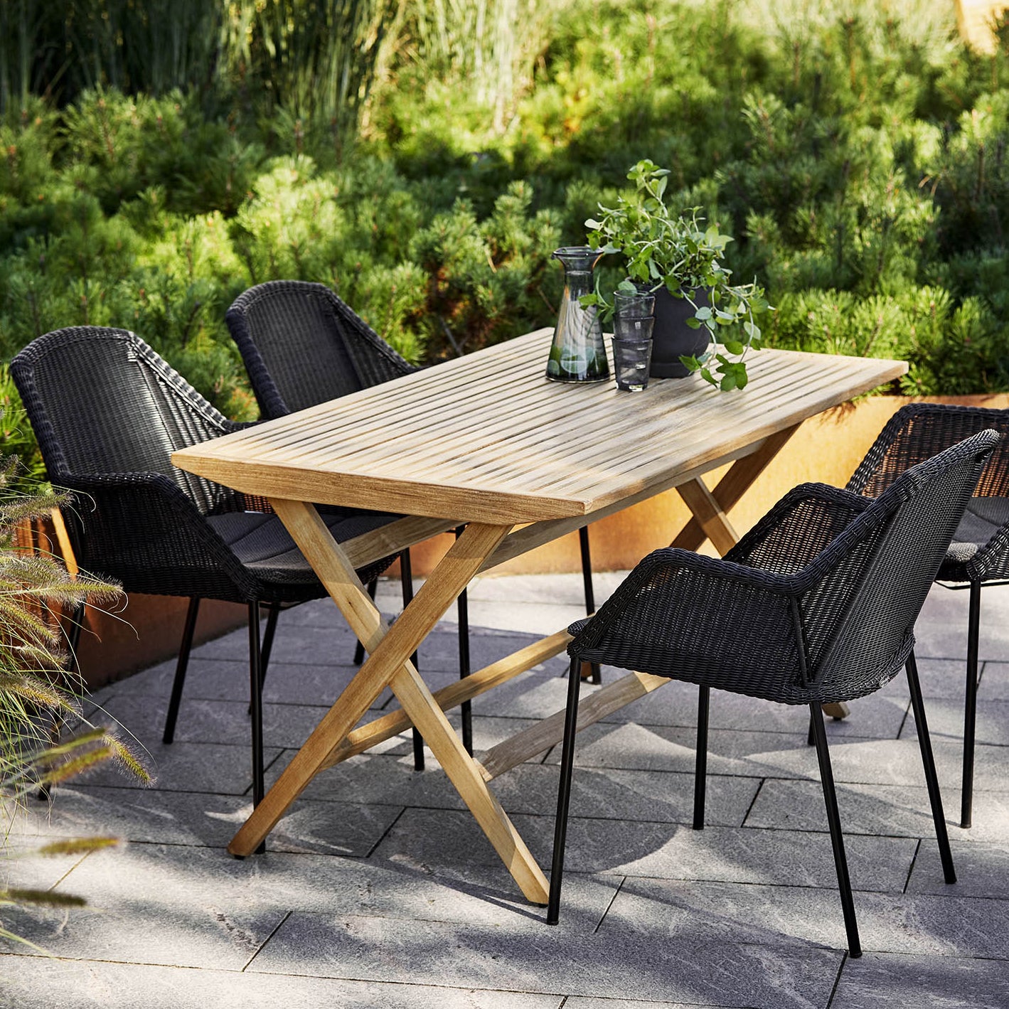 Cane-line wooden slatted dining table set with black chairs, sustainable garden furniture Comosum
