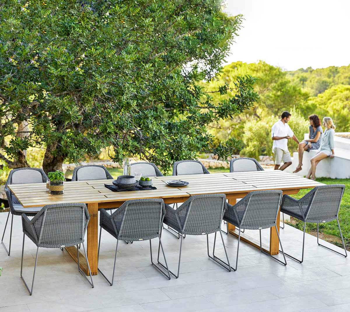Cane-line Endless Dining Table set for a meal with gray dining chairs, styled in a garden, solid teak