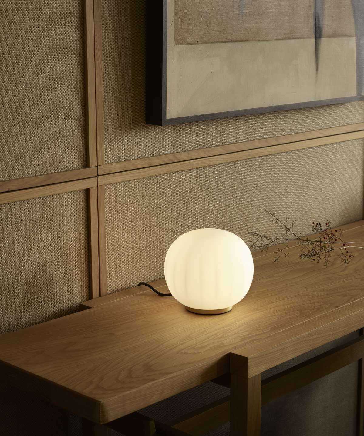 Luceplan Lita Stemless Table Lamp with a brass base, lit on a wooden desk