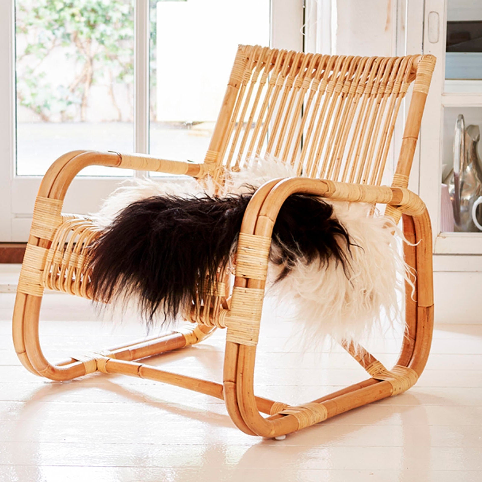 Cane Line Curve Lounge Chair Wicker chair with a fluffy cushion on a light wooden floor.