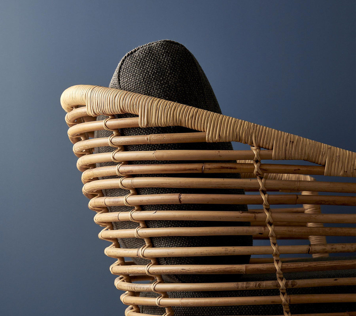 Cane-line Sense Lounge Chair in natural rattan against a blue backdrop, shown with a cushion set