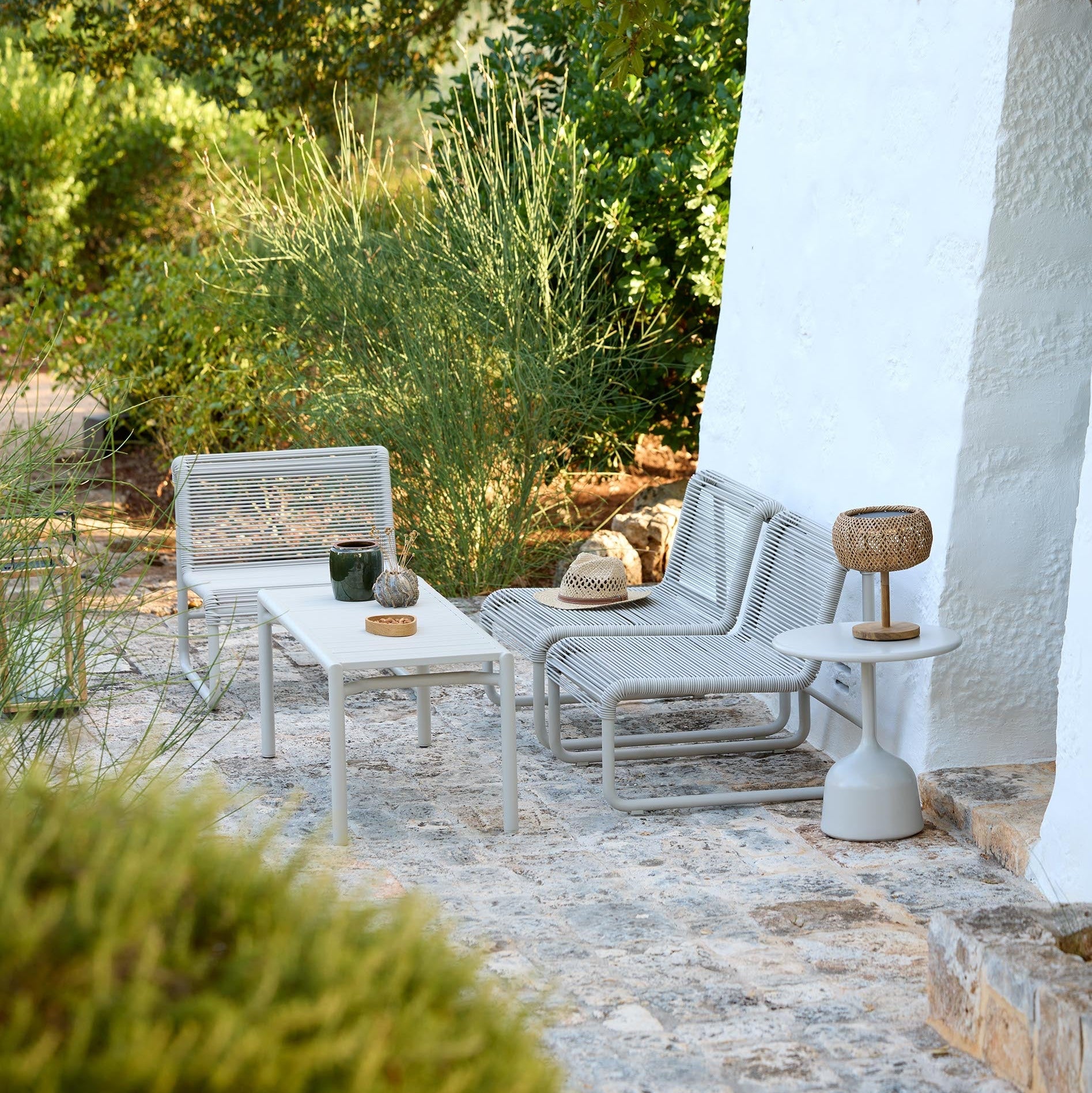 Outdoor patio with white furniture, table, and decorative items under a tree.