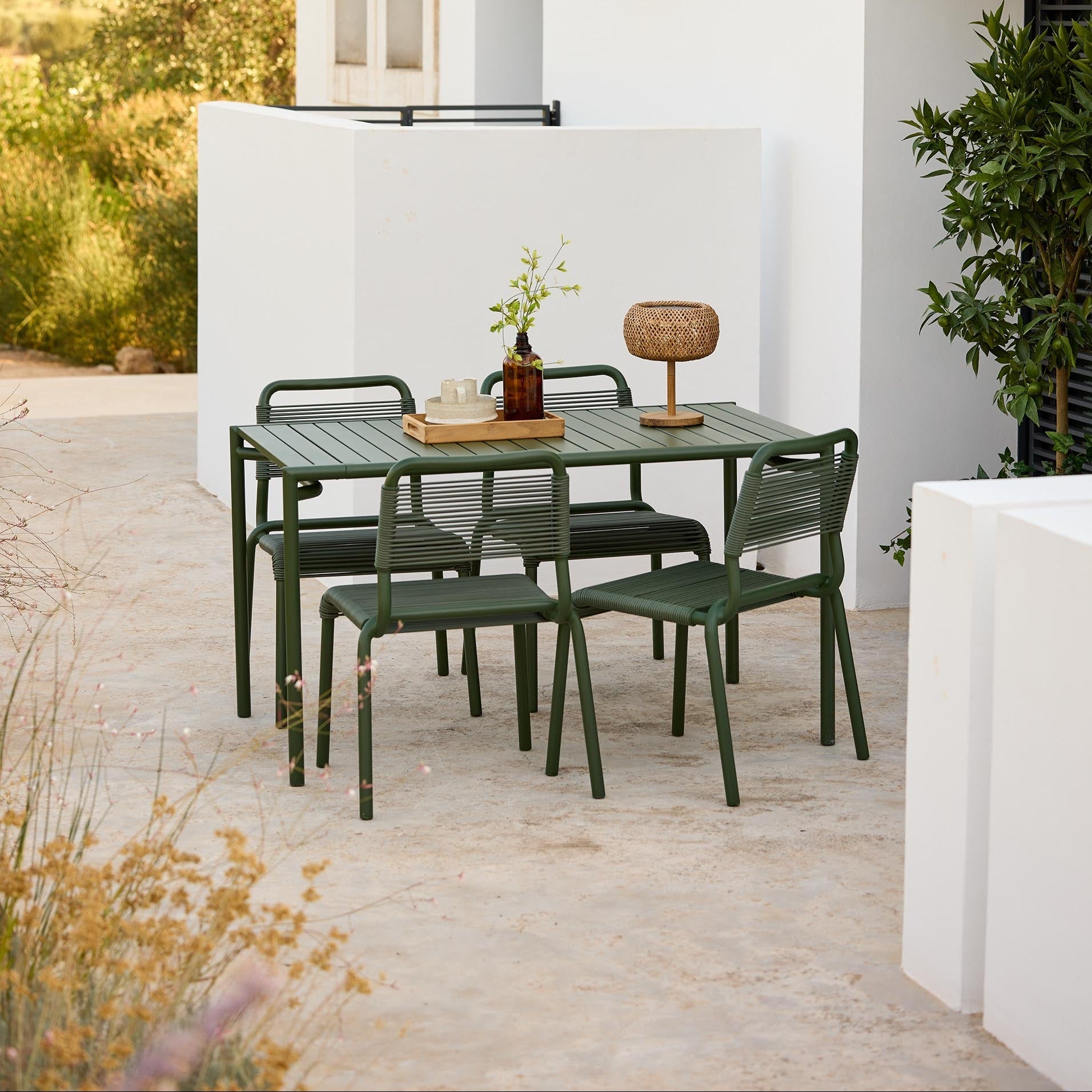 Outdoor dining set with green table and chairs on a patio in front of a white building.