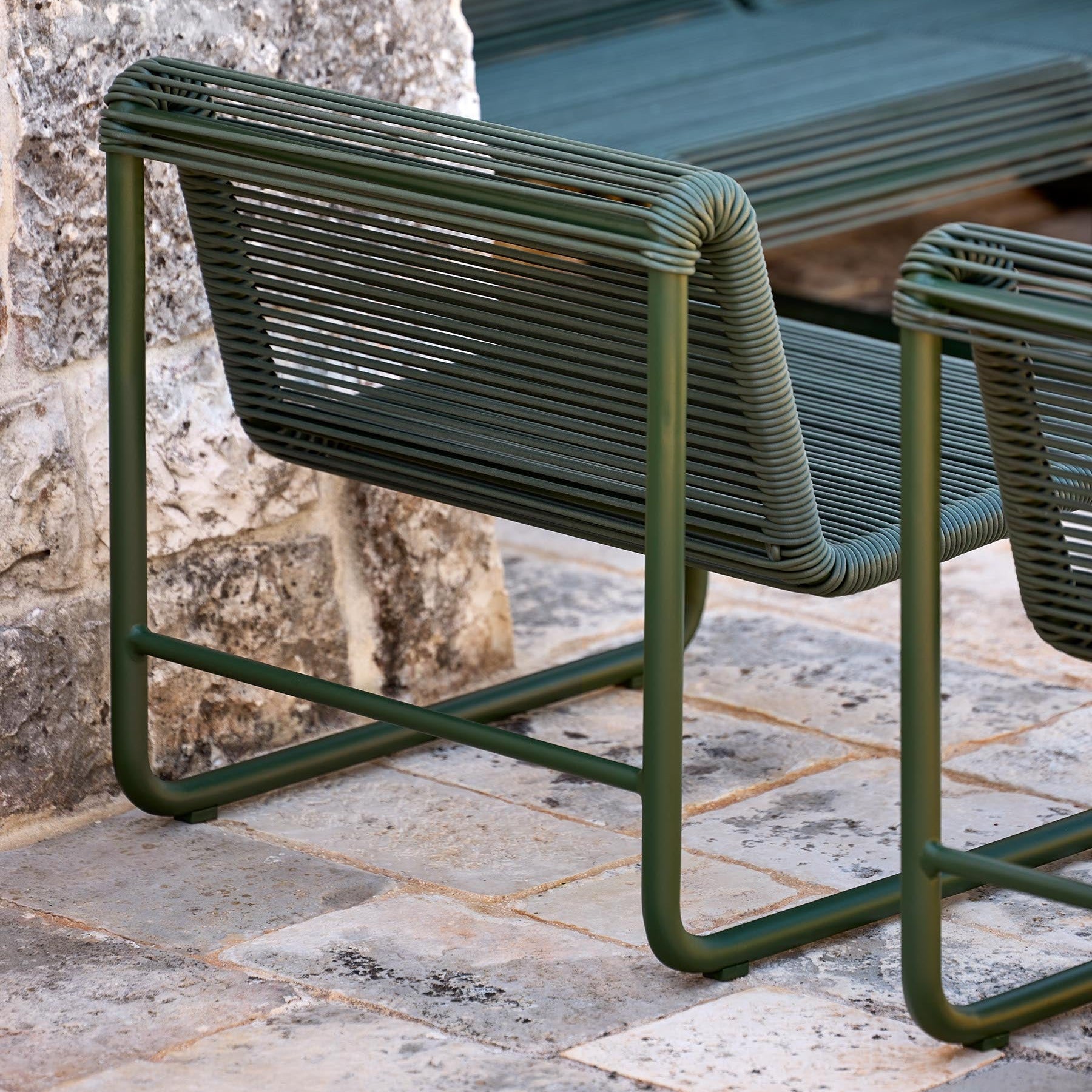 Green outdoor chair on a stone pavement with a stone wall in the background