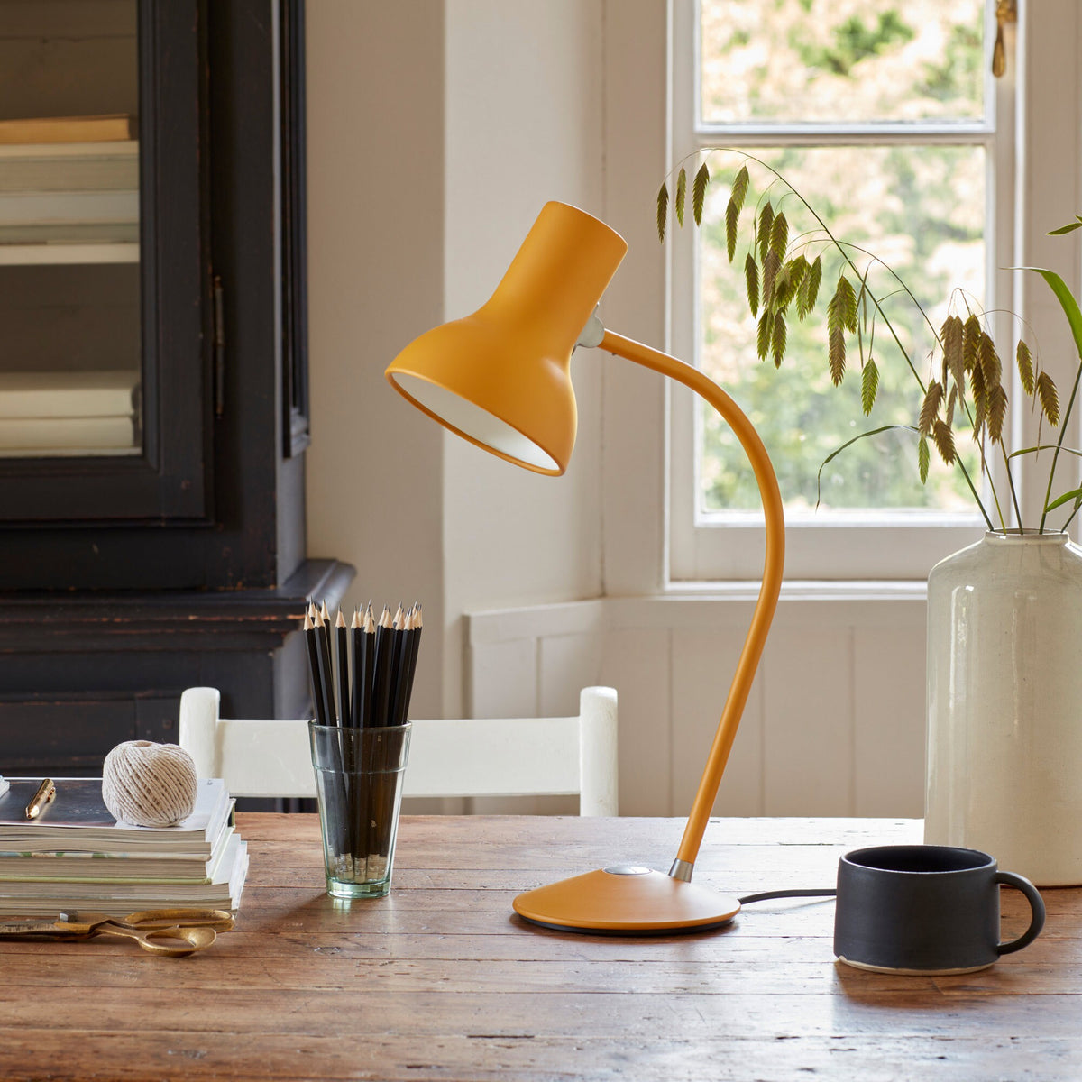 Anglepoise Type 75 Mini table lamp in Turmeric Gold on a wooden table by a window