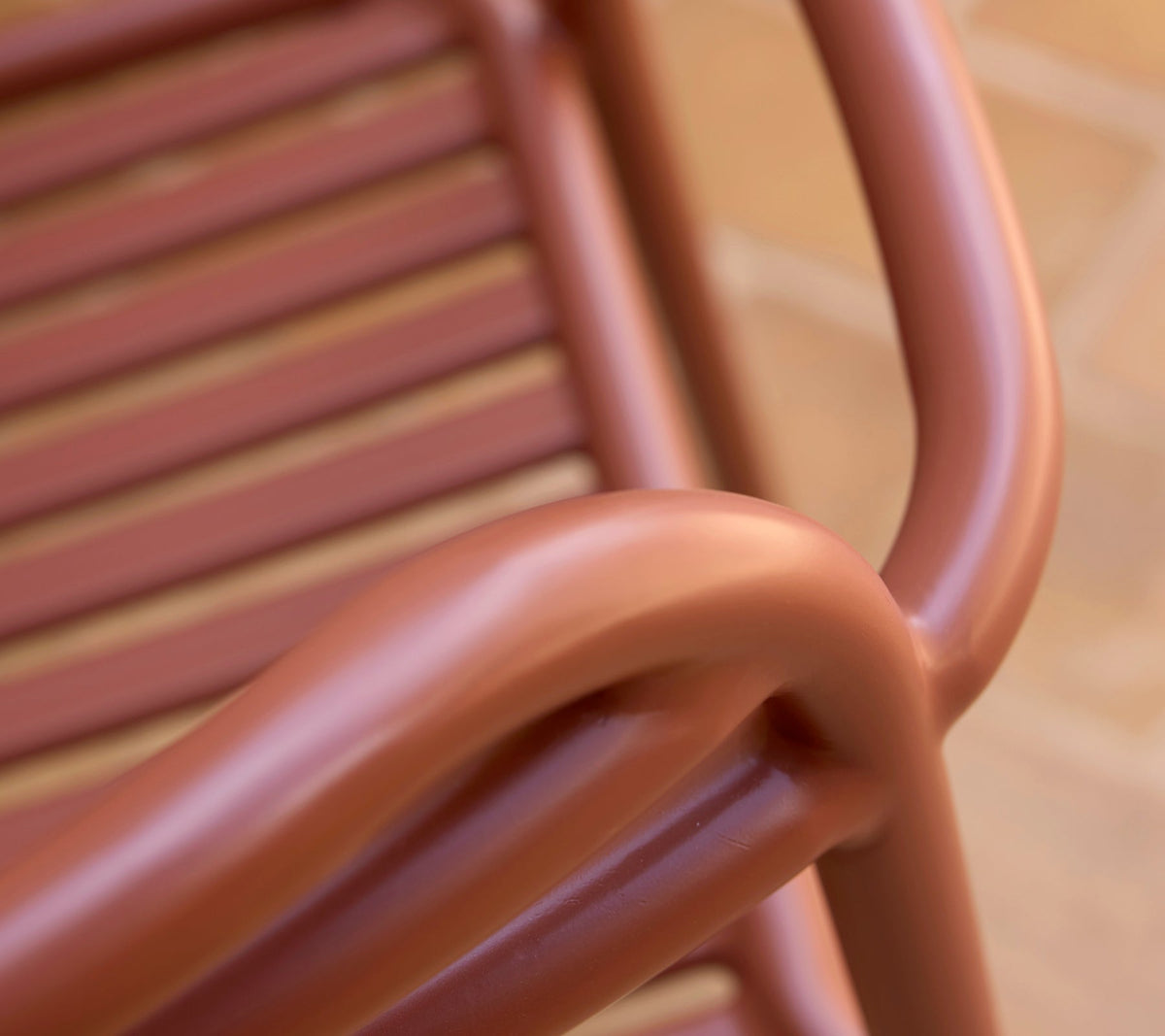 Detail of Cane-line Bliss armchair in Desert Red showing its curved arm and slatted back, powder-coated aluminum