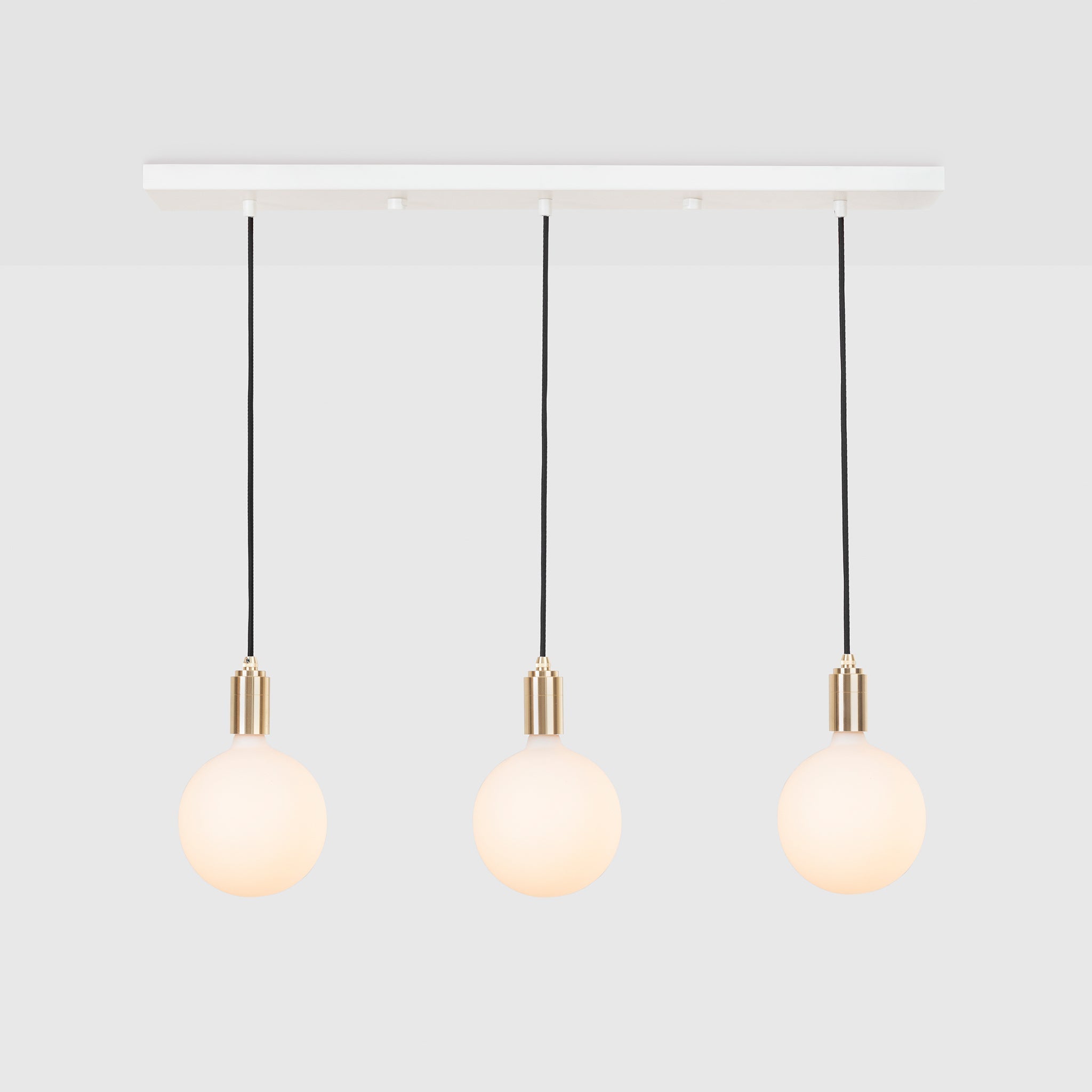 Tala Linear Triple Pendant in Brass with Sphere IV bulbs, on a plain grey background