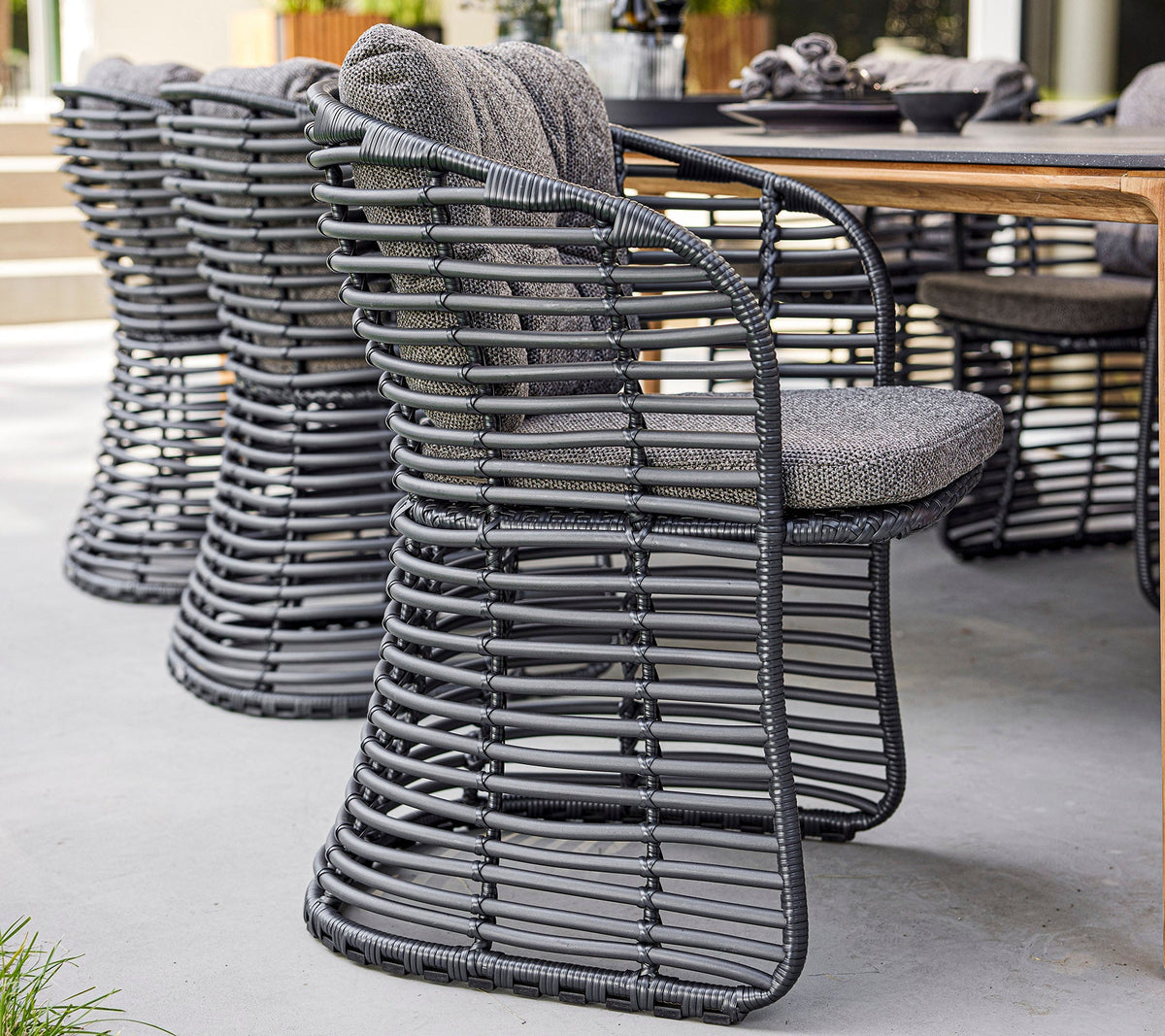 Cane-line Basket Dining Chairs in hand-woven Cane-line Weave beside a wooden table, styled outdoors