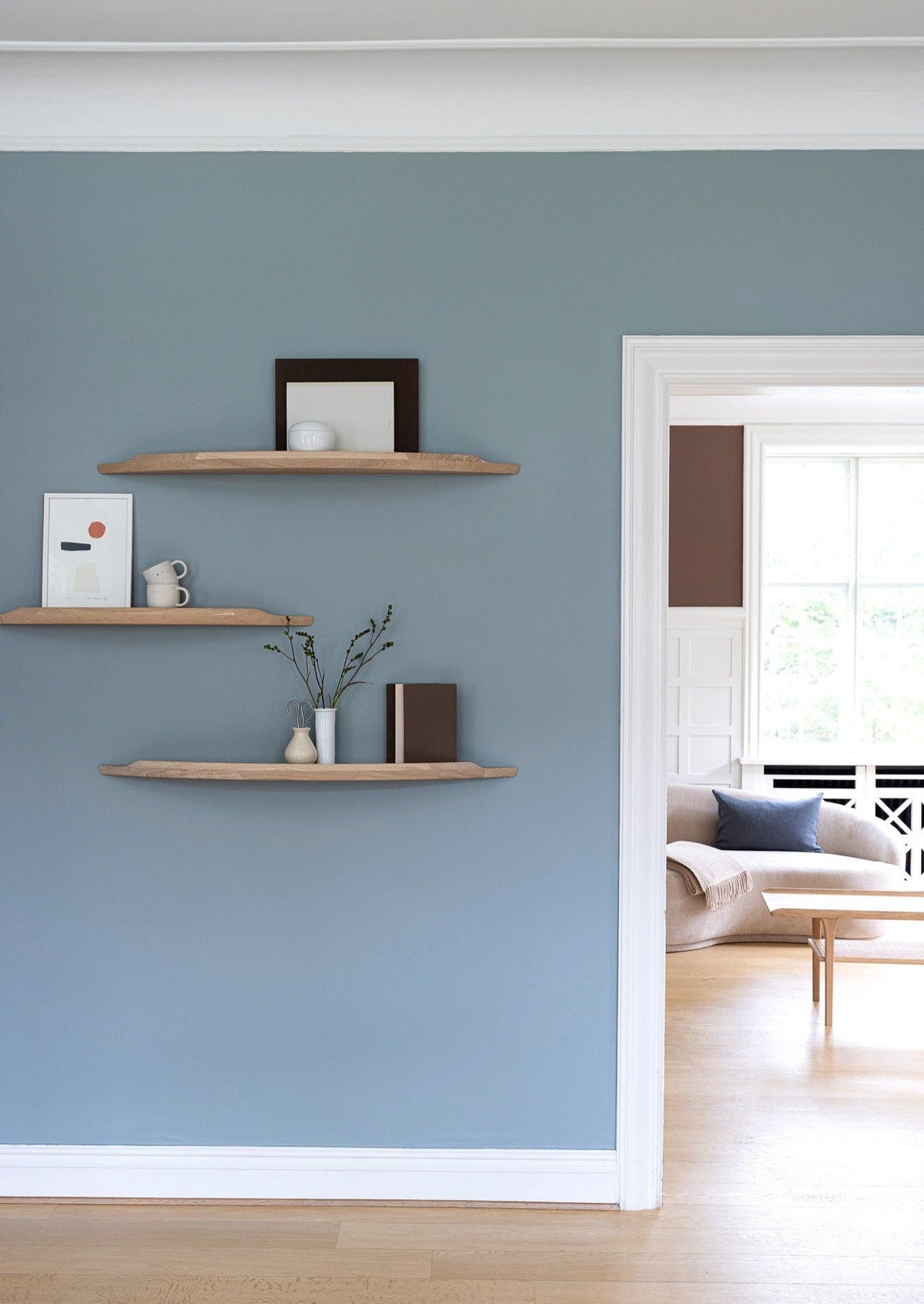 Aakjaer Arcus shelves in white oiled oak hung at staggered heights in a blue living room