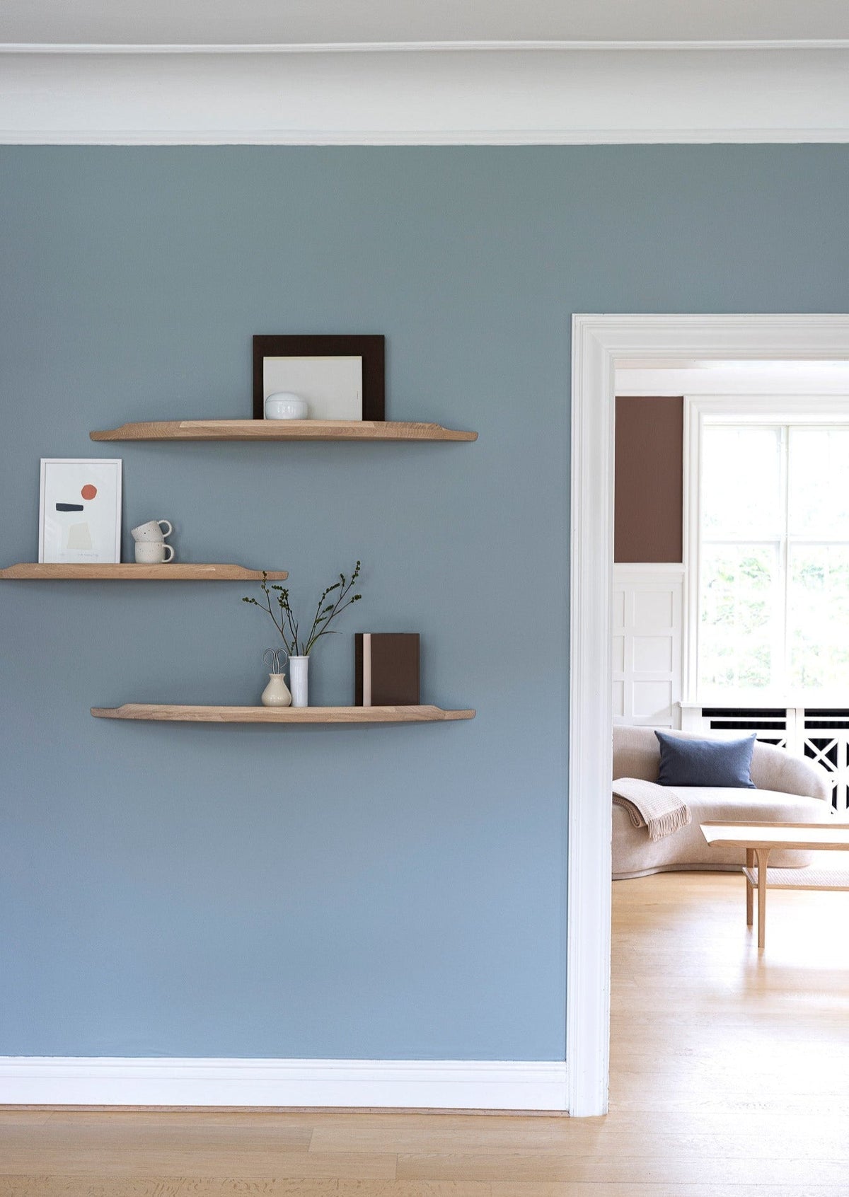Aakjaer Arcus shelves in white oiled oak hung at staggered heights in a blue living room