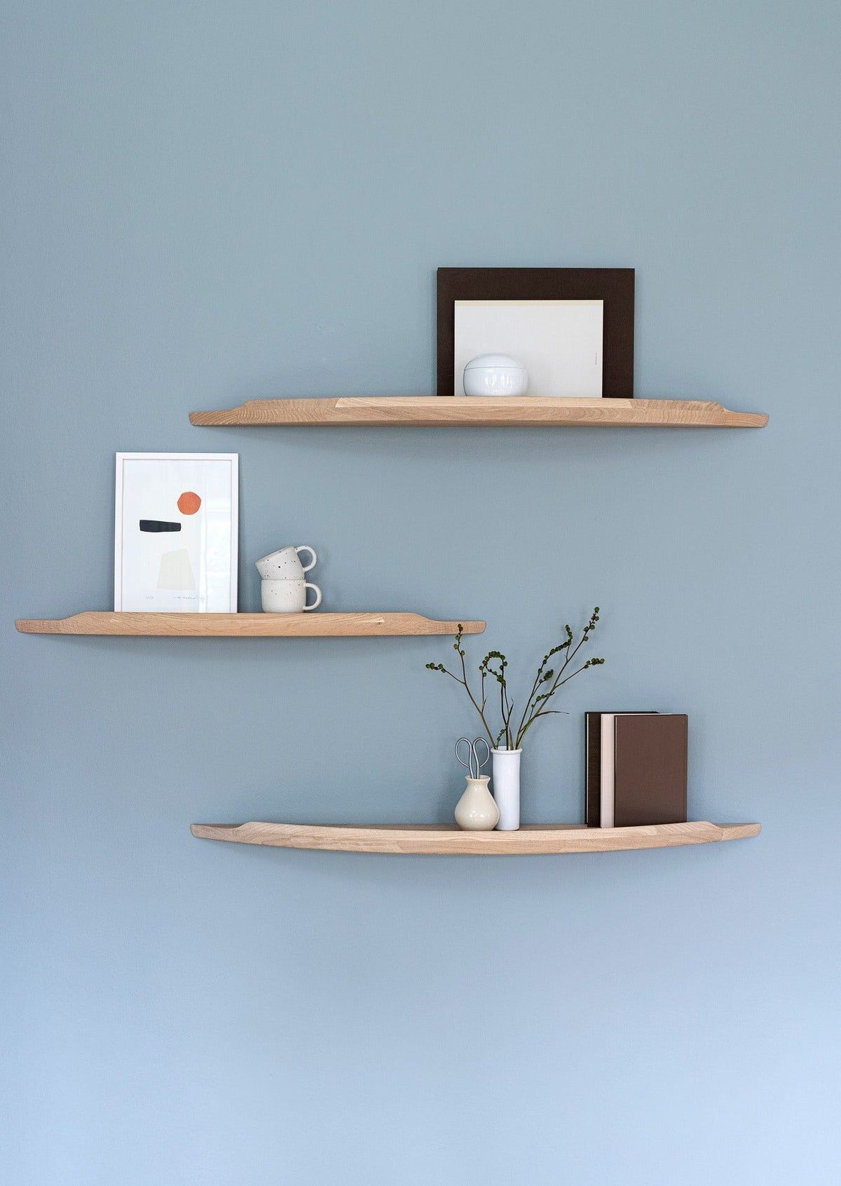 Three Aakjaer Arcus shelves in white oiled oak with prints and ceramics on a blue wall