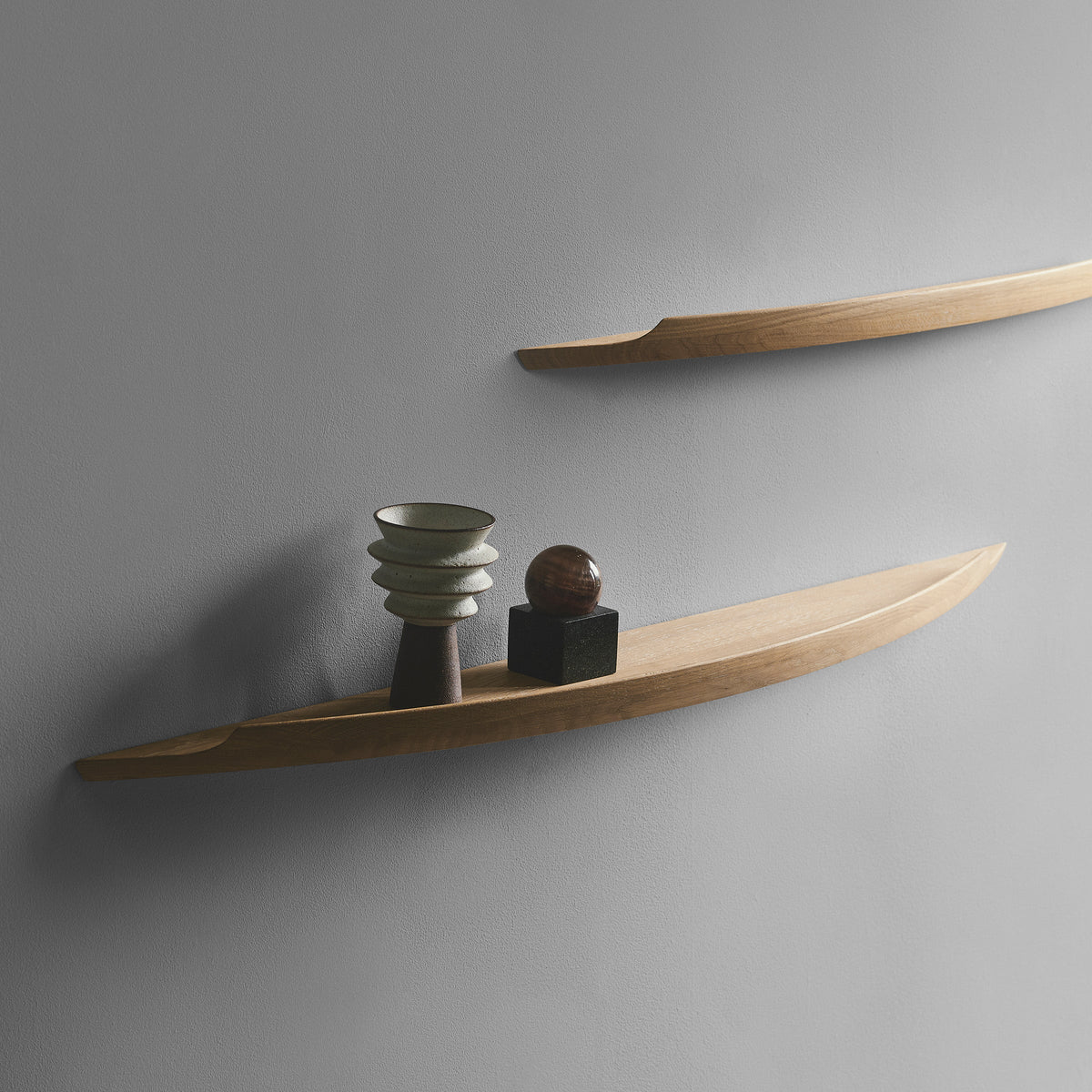 Aakjaer Arcus shelves in white oiled oak on a gray wall, styled with small ceramics