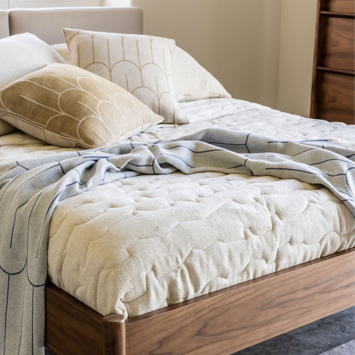 Case Ripple quilt in off-white on a walnut bed with patterned cushions