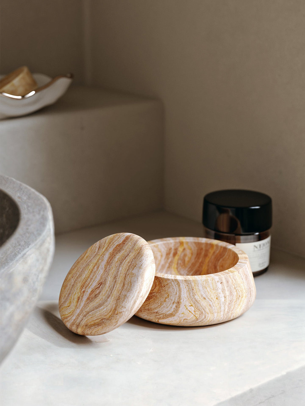 WOUD Serene Jar, Low, in Rainbow Sandstone with its lid set aside, styled on a stone ledge, solid natural stone