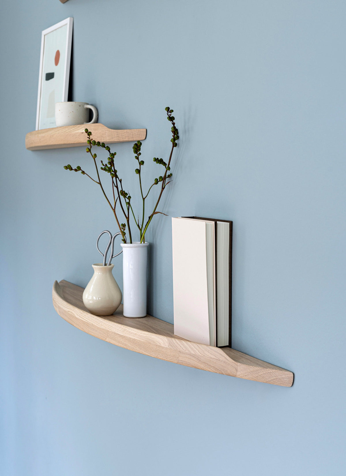 Aakjaer Arcus shelves in white oiled oak with vases and books on a blue living room wall