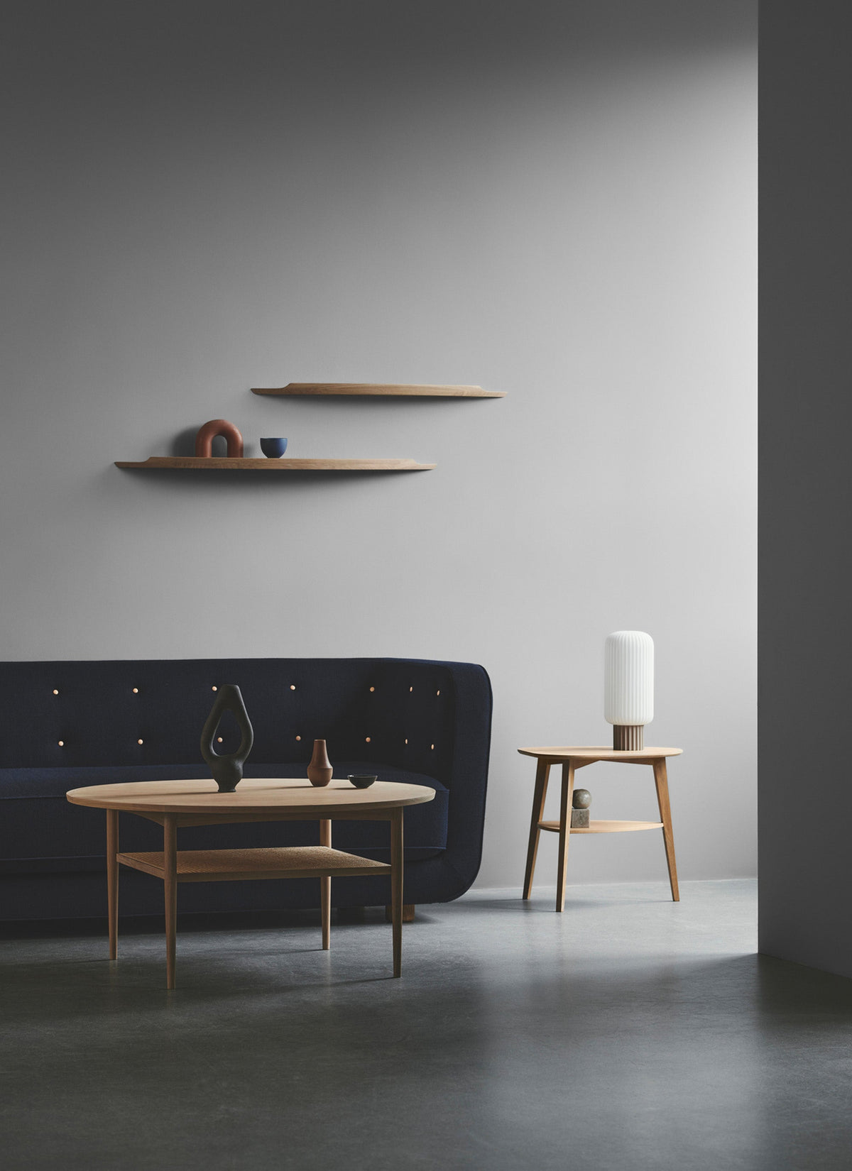 Two Aakjaer Arcus shelves above a sofa and an oak coffee table in a gray living room