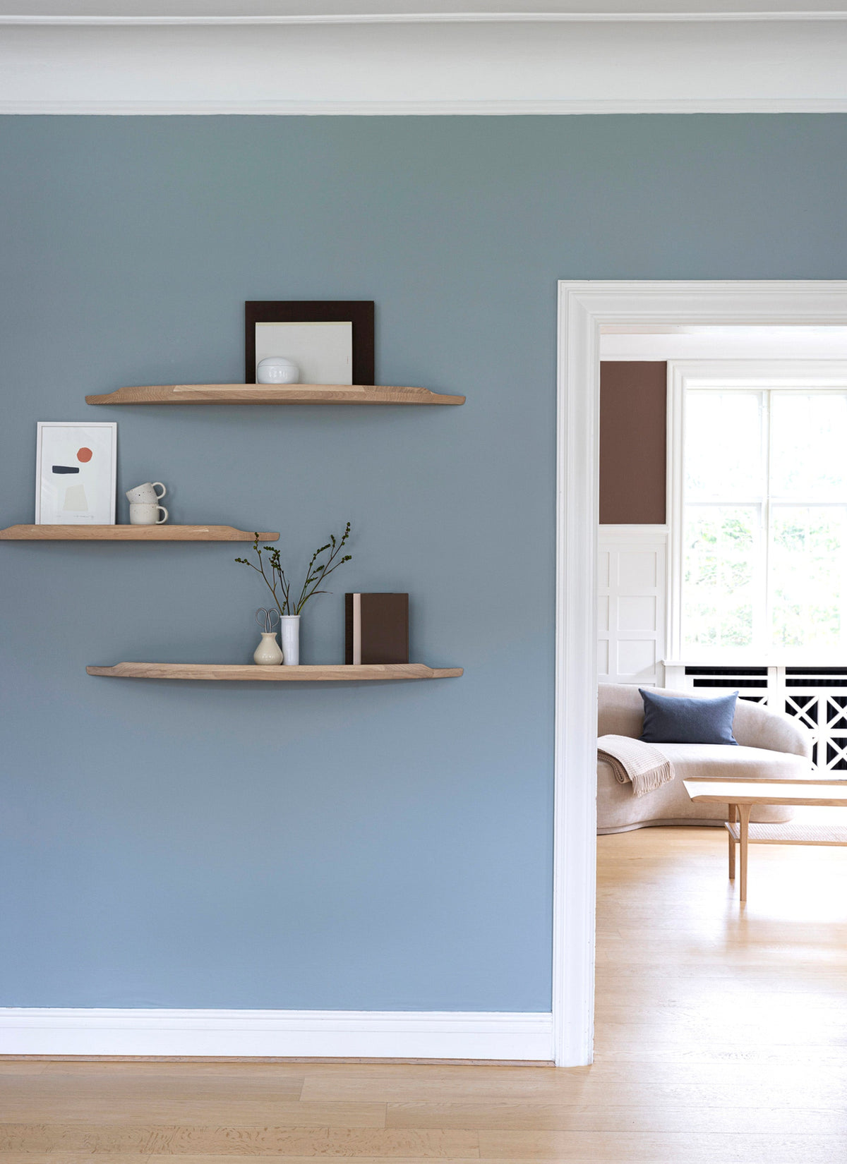 Three Aakjaer Arcus shelves in white oiled oak hung at staggered heights in a blue living room