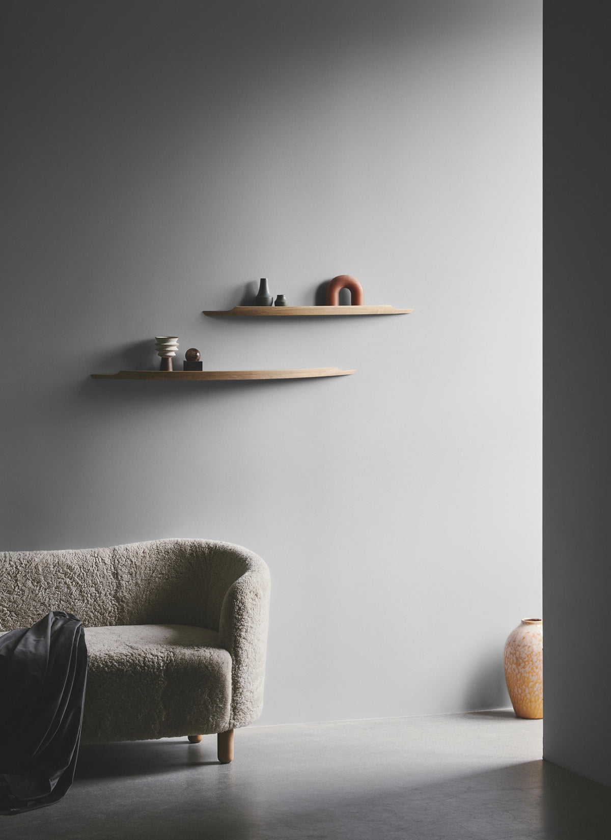 Aakjaer Arcus shelves on a gray wall beside a boucle armchair
