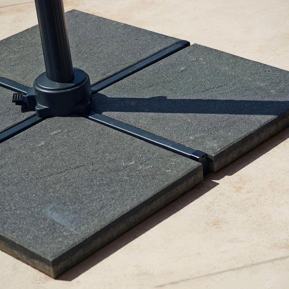 Four Cane-line Hyde Luxe parasol base tiles in gray holding a parasol pole