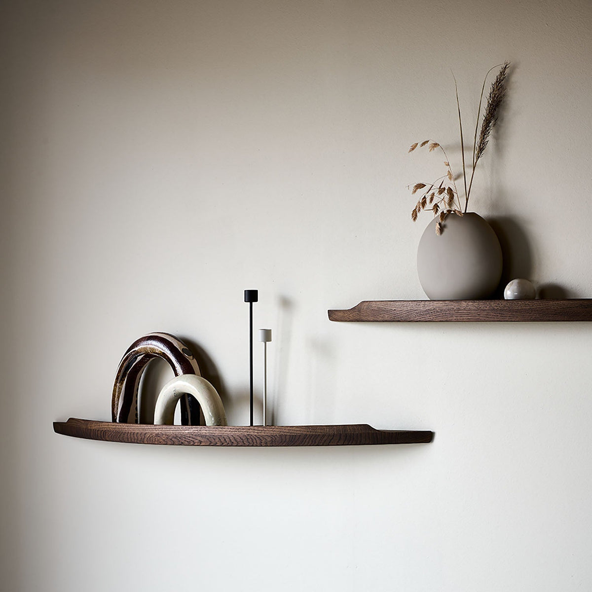 Two Aakjaer Arcus shelves in smoked oak styled with ceramic arches, candlesticks and a vase