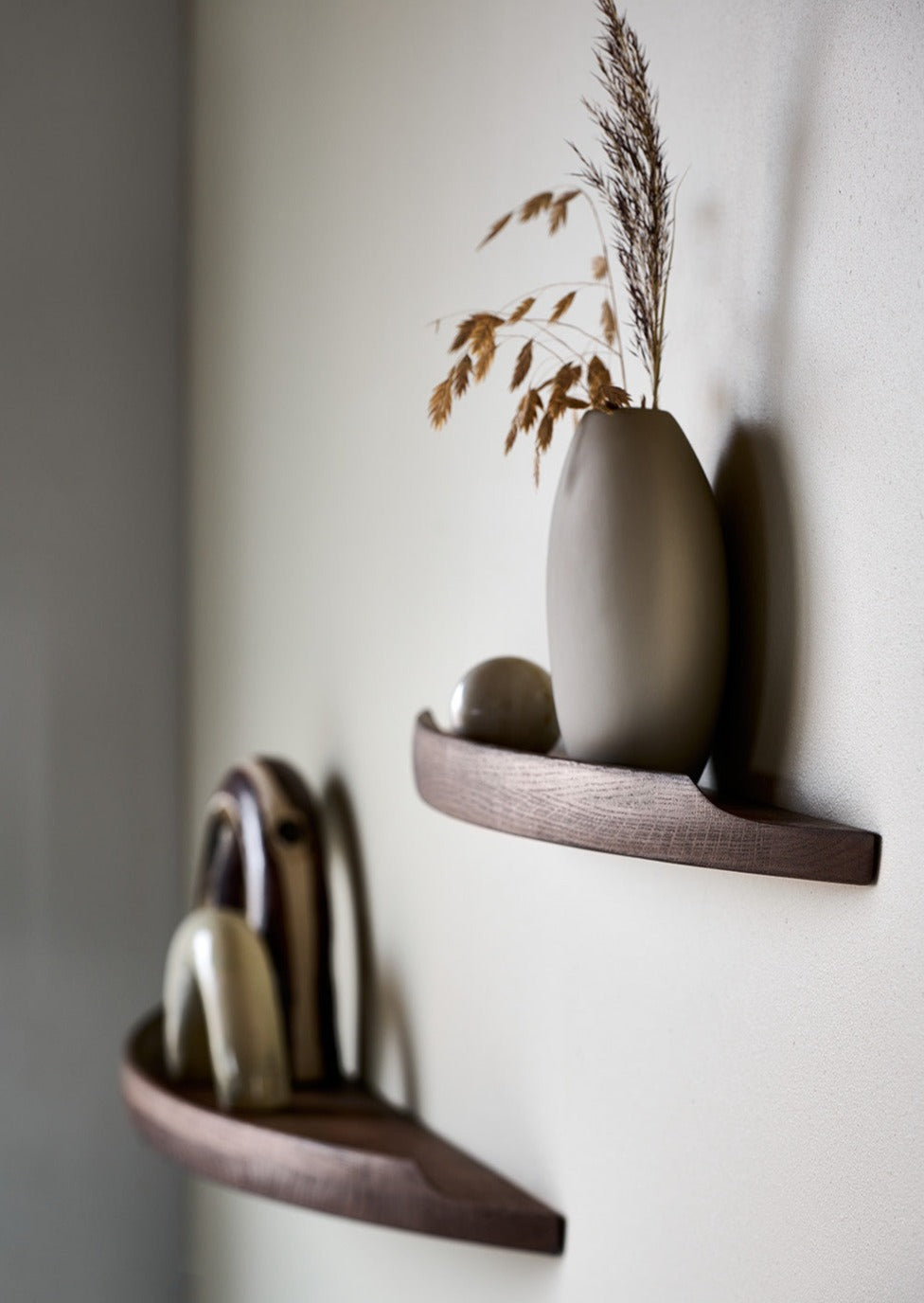 Side view of Aakjaer Arcus shelves in smoked oak holding ceramics and a tall vase