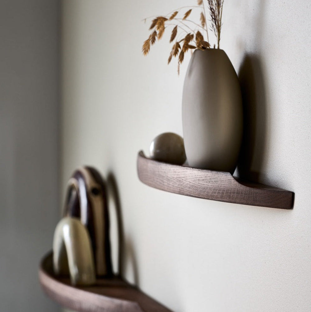 Side view of Aakjaer Arcus shelves in smoked oak holding ceramics and a tall vase