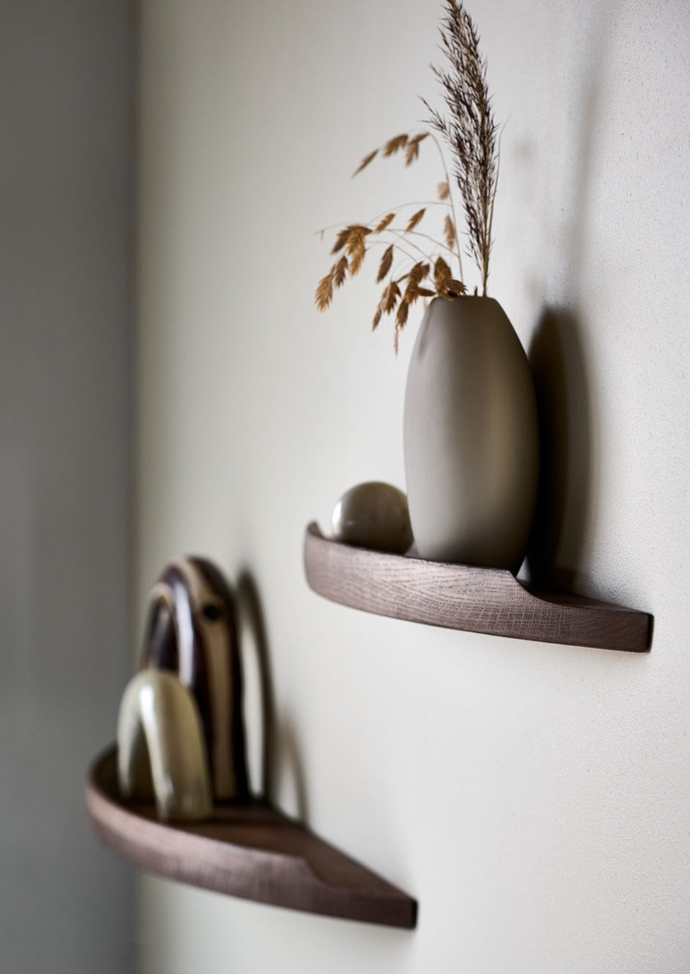 Side view of Aakjaer Arcus shelves in smoked oak holding ceramics and a tall vase