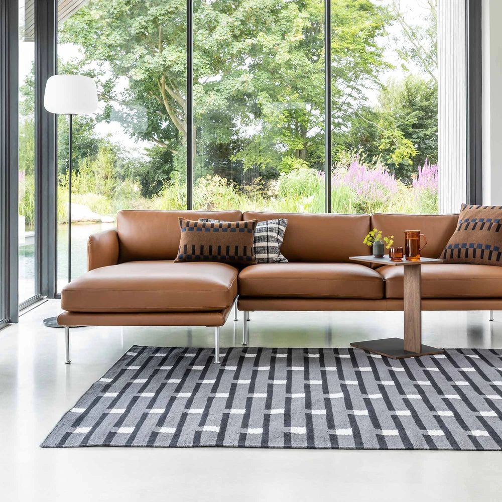 Case Purlin rug in black in front of a brown leather sofa in a glass-walled living room