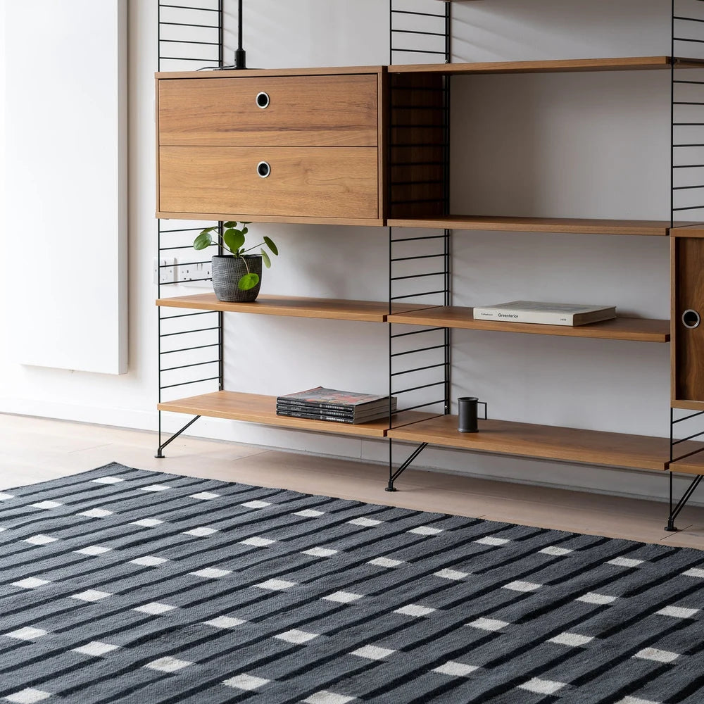 Case Purlin rug in black in front of wall-mounted wooden shelving
