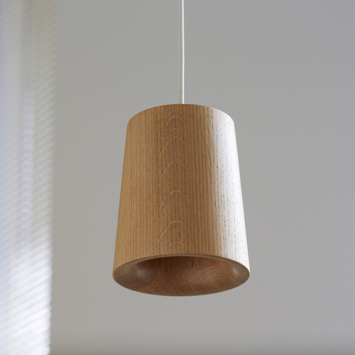 Case Solid Pendant cone in Oak, styled against a gray wall, solid oak