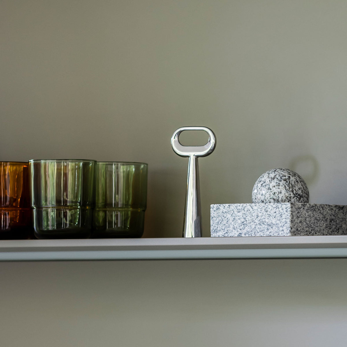Case Stand Bottle Opener in polished stainless steel, styled on a shelf with glassware