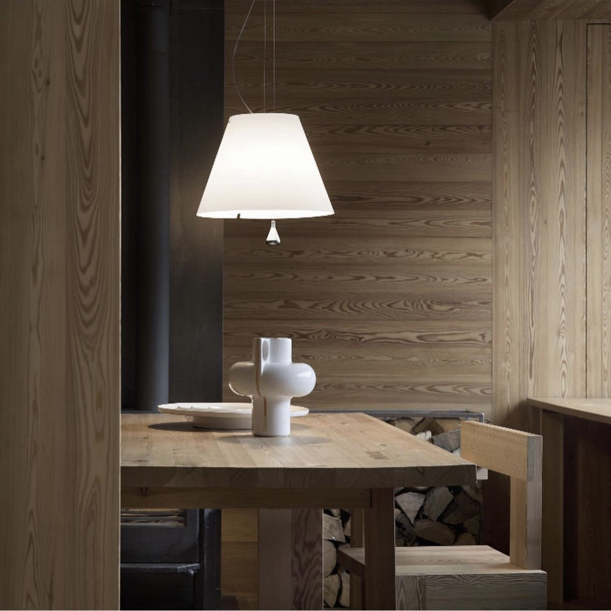 Luceplan Costanza Pendant with a white shade over a wood dining table, styled in an interior setting