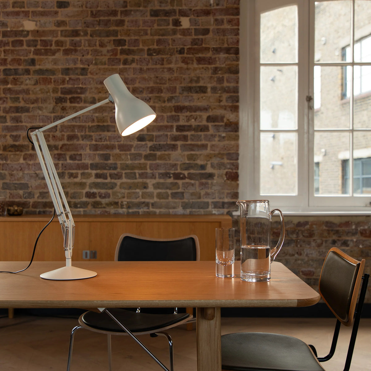 Anglepoise Type 75 desk lamp in Alpine White on a wooden dining table in a brick-walled room