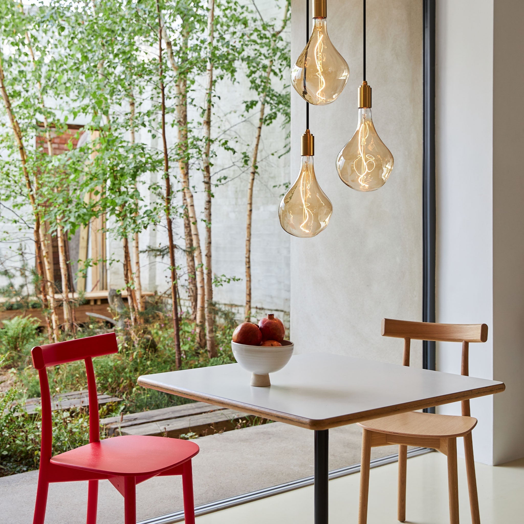Tala Triple Pendant in Brass with Voronoi II bulbs — indoor/outdoor living lifestyle with chairs
